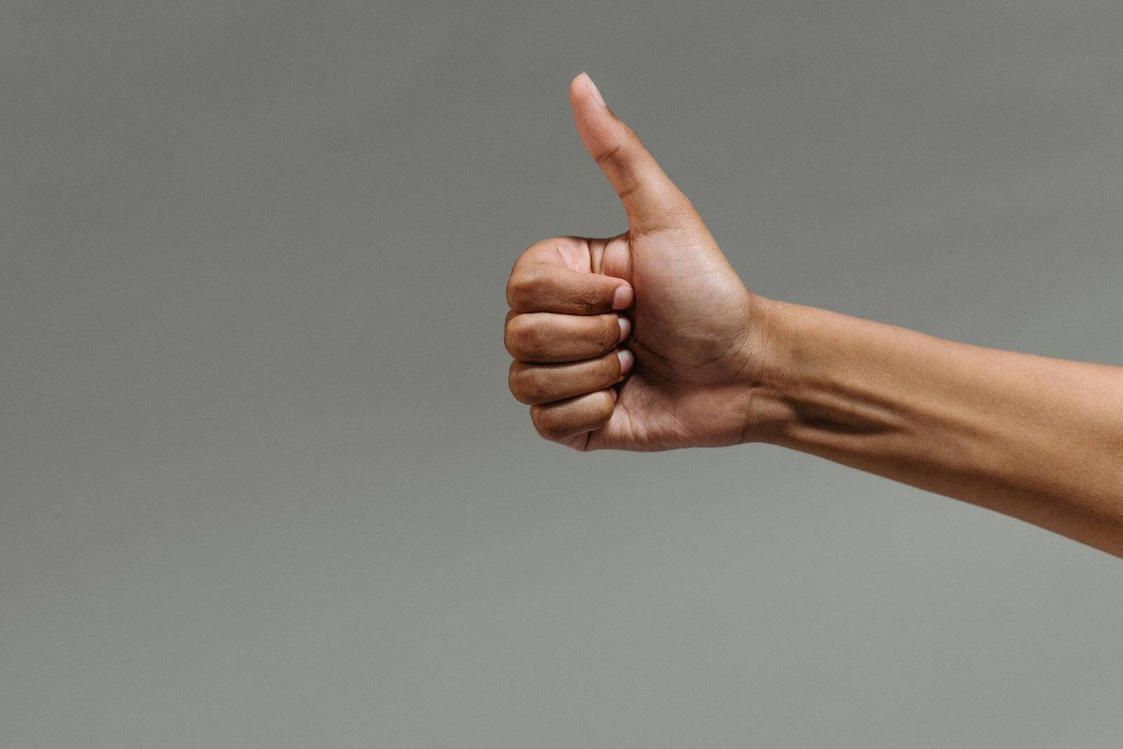A close-up image of a hand making a thumbs up gesture against a neutral background.