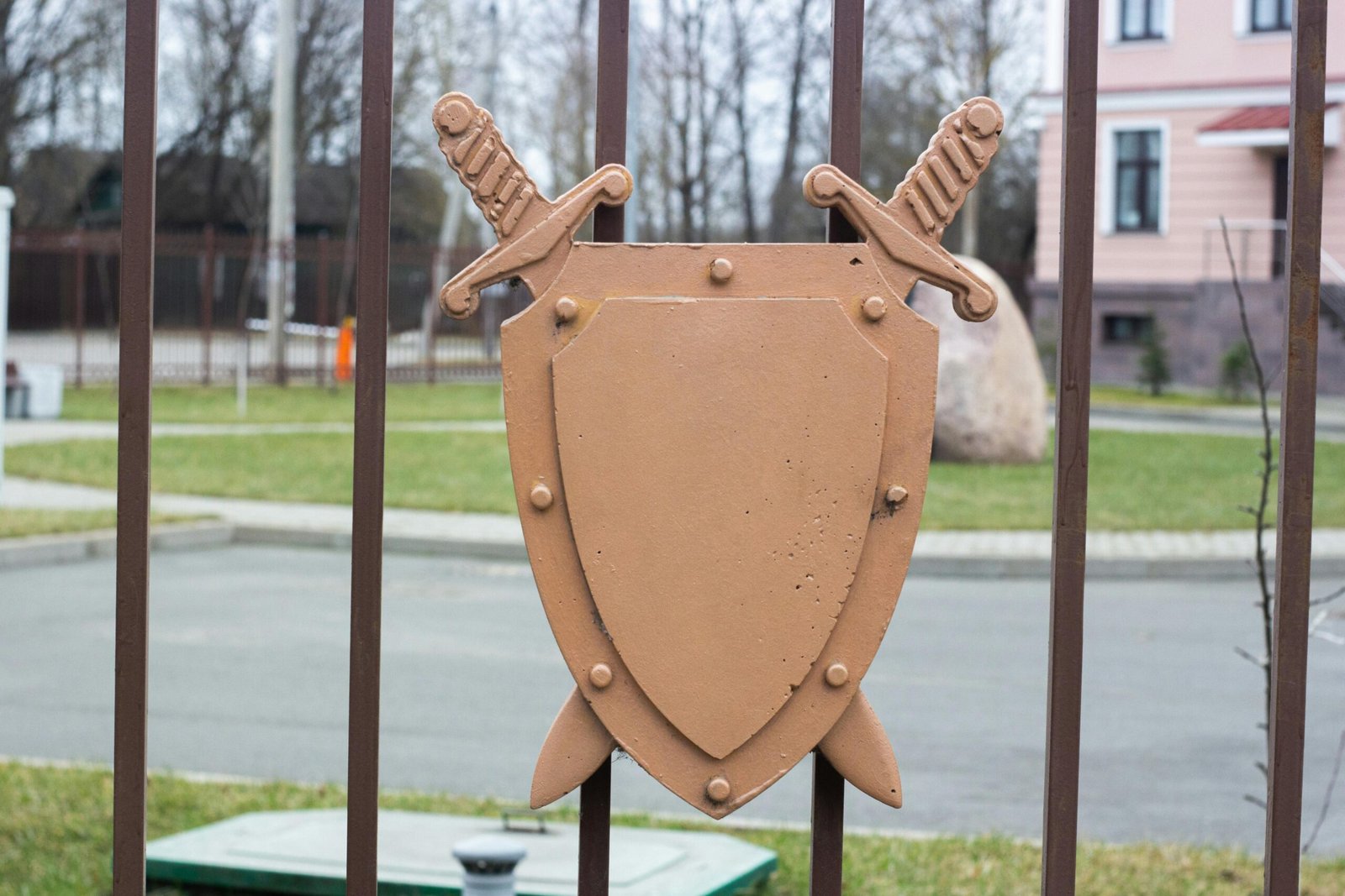 Decorative shield and swords on a metal fence in a residential area.